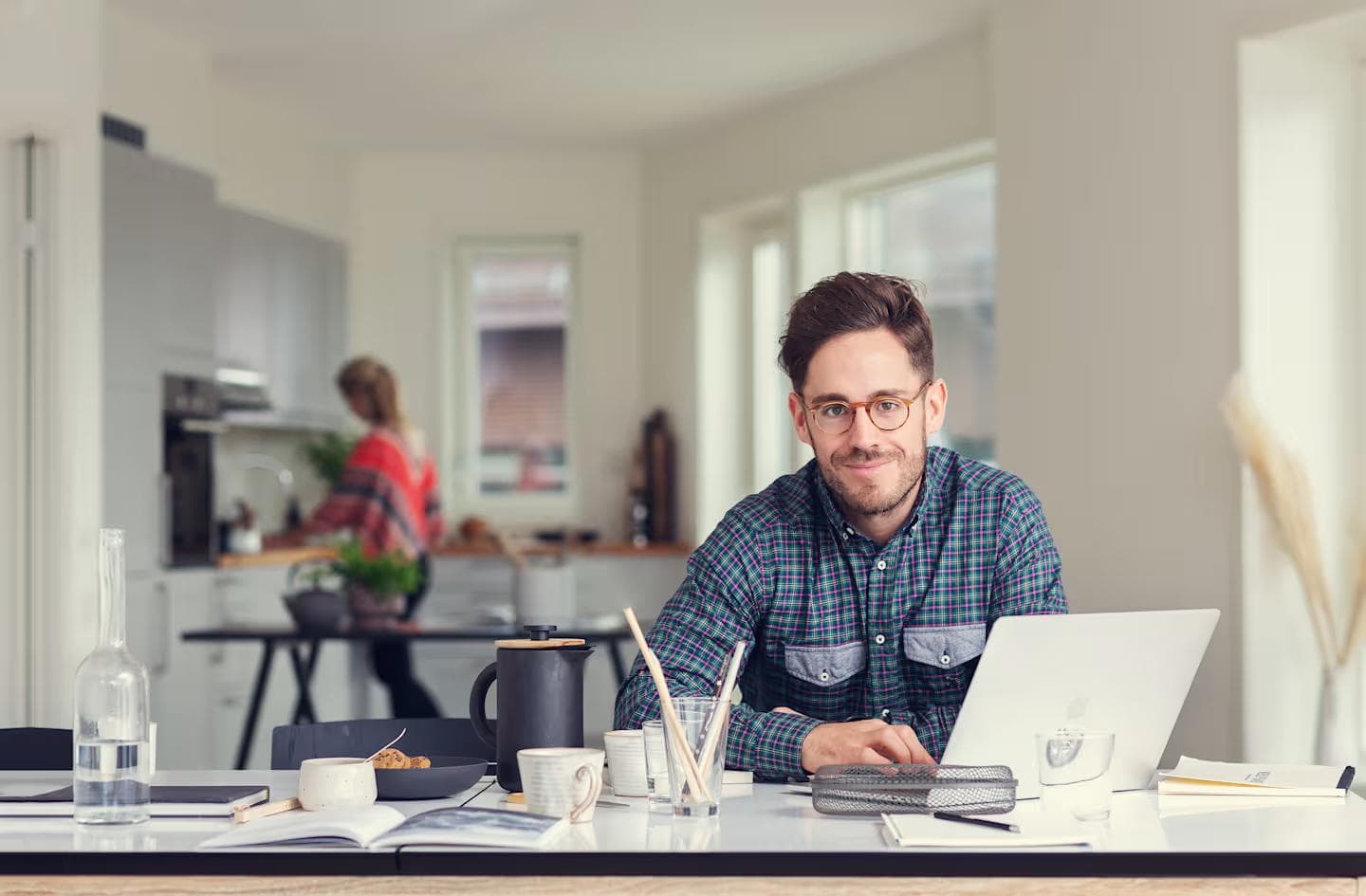 Mann ved skrivebord med laptop og kaffekopp som smiler mot kameraet